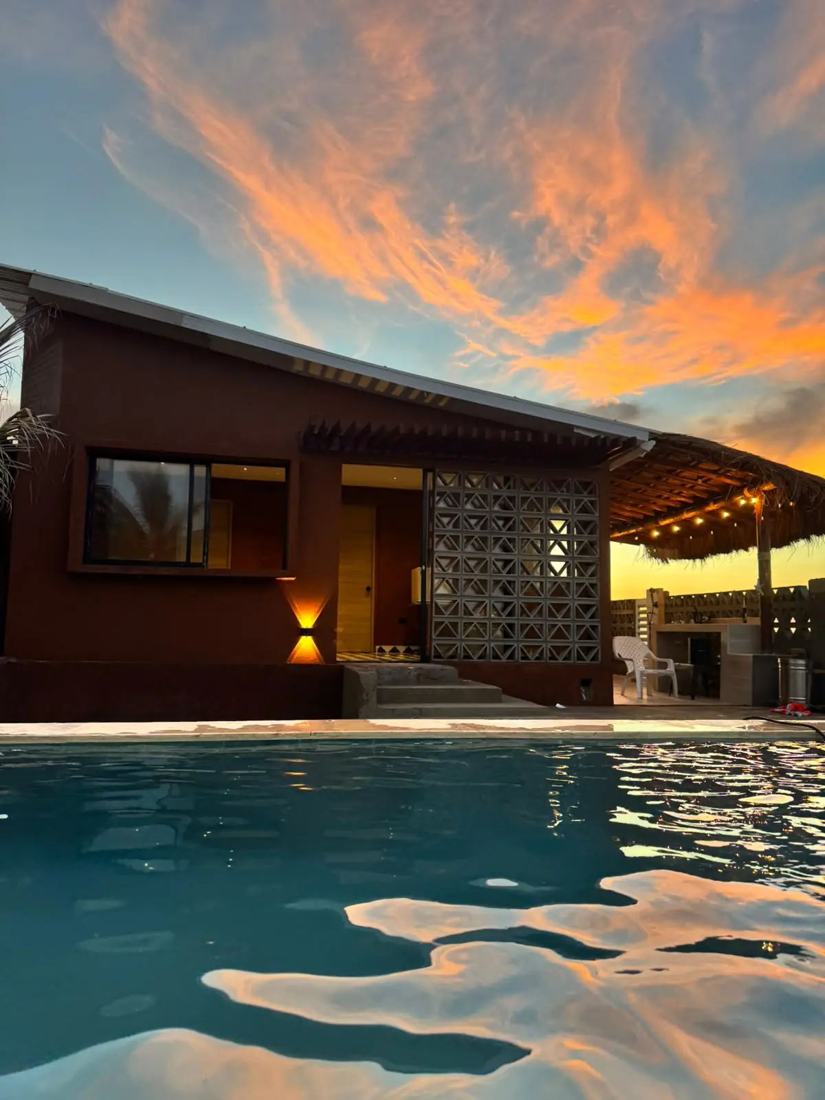 Fachada de una cabaña de Mokano con celosía de bloque y cielo anaranjado al atardecer